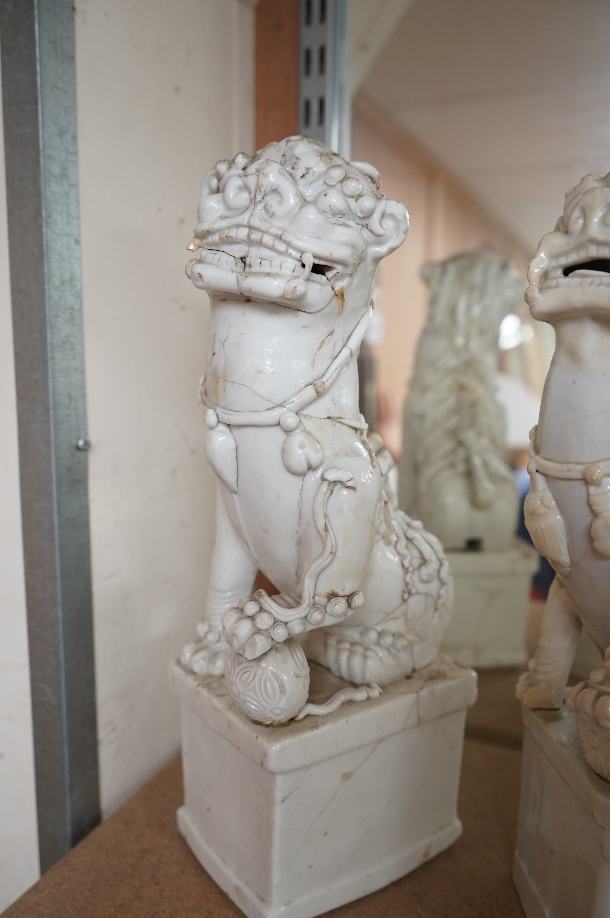 Two large Chinese Dehua blanc de chine Buddhist lion joss-stick holders, Kangxi period, each seated, one paw raised on a ball, on rectangular pedestal basis, 35cm high, Condition - extensive cracks or repairs